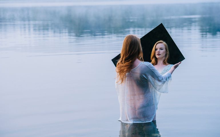 Rear view of young woman standing in lake holding mirror looking at reflection