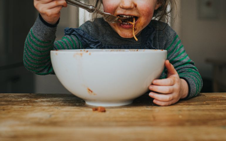 Cute young girl messily eating a big white bowl of Spaghetti Bolognese.