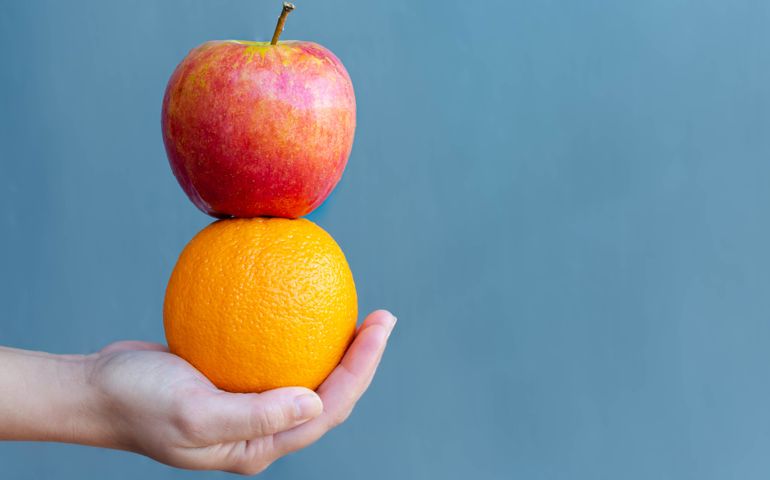 A hand holding a stack of orange and apple in front of a blue background.