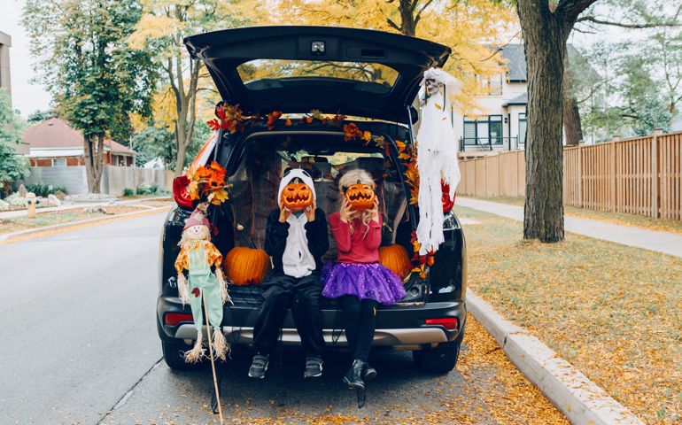 Trick or trunk. Children celebrating Halloween in trunk of car. Boy and girl with red pumpkins celebrating traditional October holiday outdoor. Social distance and safe alternative celebration.