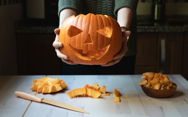 WOMAN IN FRONT OF A TABLE HOLDING A CARVED PUMPKIN ON THE OCCASION OF HALLOWEEN
