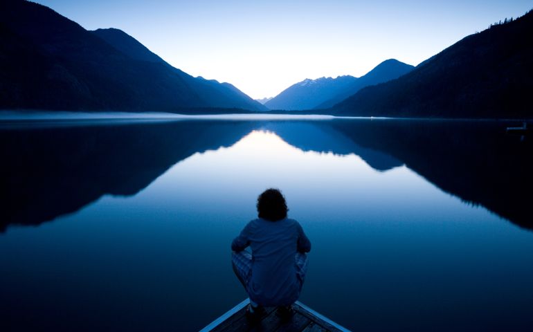 Person sitting quietly on the edge of a dock watching the sunset