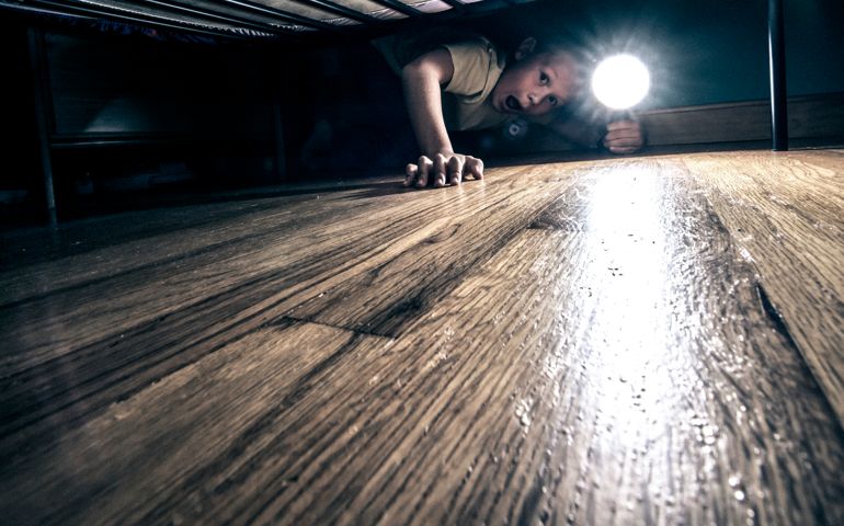 Very scared little boy looking under his bed using flashlight in search of monsters and demons that may lurk in the darkness at night. Grain added.