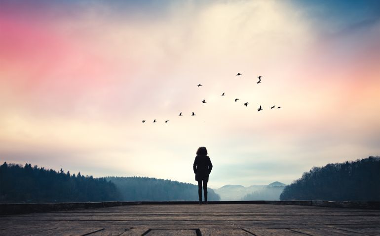 Woman standing on jetty and watching sunrise by the lake.