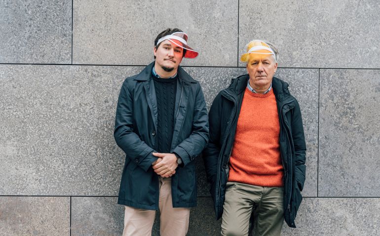 Portrait of young man and senior man wearing sun visors leaning against a wall