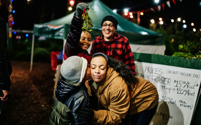 Son kissing mother on cheek under mistletoe while shopping for Christmas tree