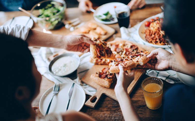 Close up of a young group of friends passing and serving food while enjoying together. They are having fun, chatting and feasting on food and drinks at dinner party