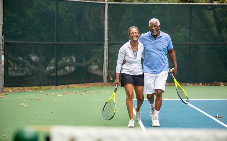A senior black couple together on the tennis court.