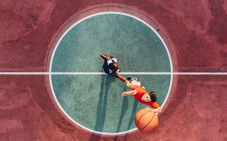 Two friends are jumping to take a basketball ball on the center field. Aerial point of view.
