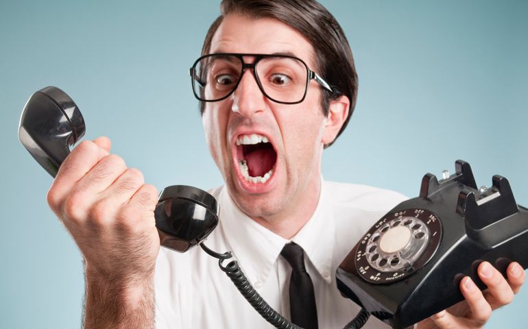 Nerdy office worker in short sleeved shirt, with attitude, holding a black rotary vintage phone.