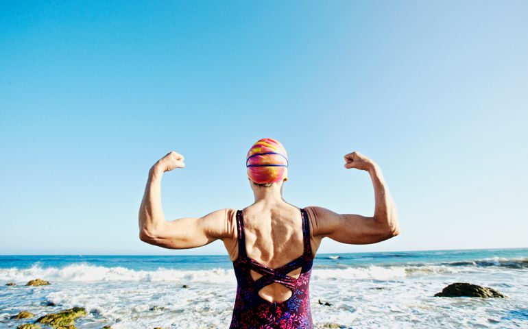 Older Caucasian woman flexing her muscles on beach