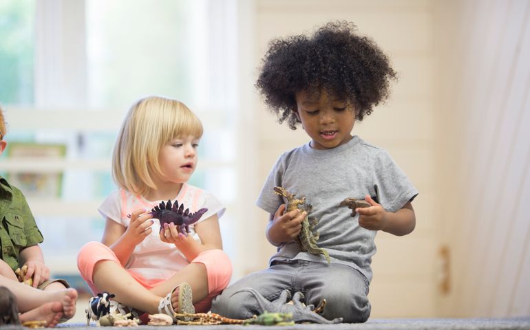 A multi-ethnic group of toddlers are playing with toy animals together in preschool.