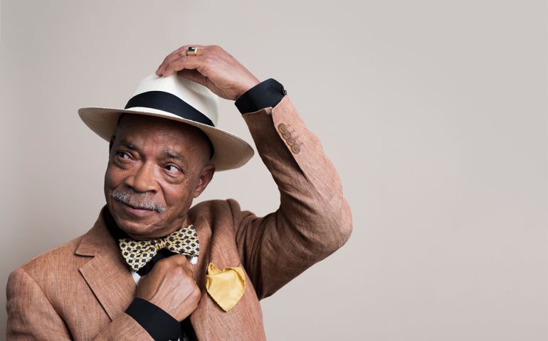 Studio portrait of a stylish senior man with a hat, in front of a beige background.