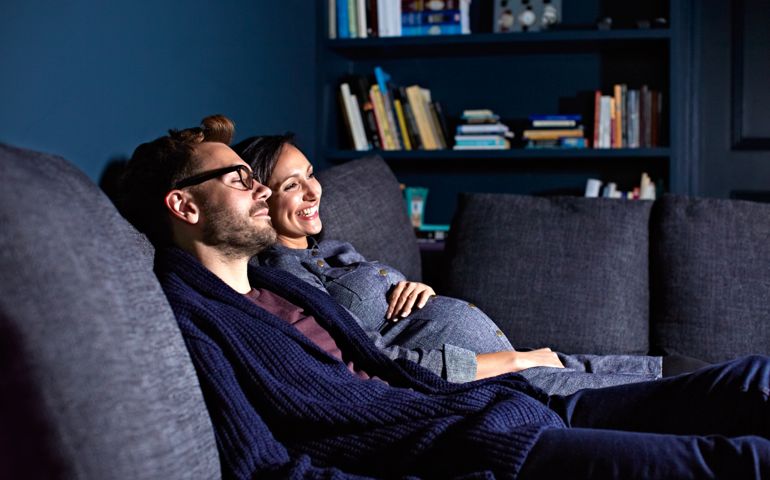 Shot of a pregnant woman and her husband sitting on the sofa watching television in the evening