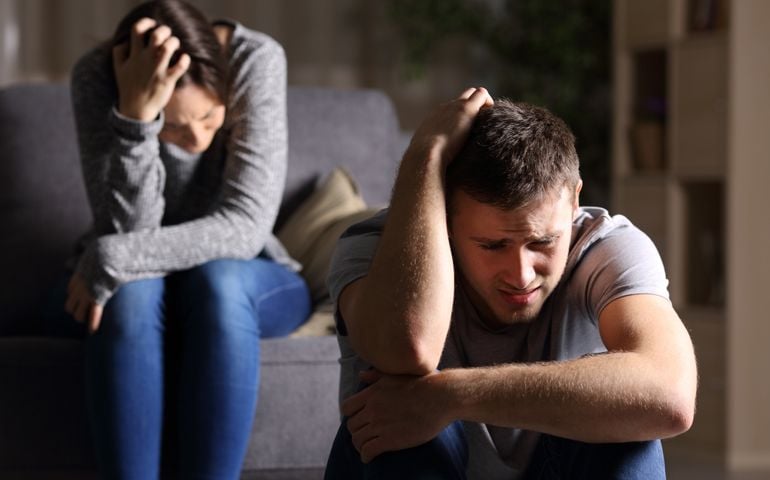 Sad couple after breaking up sitting on a couch in the living room in a house