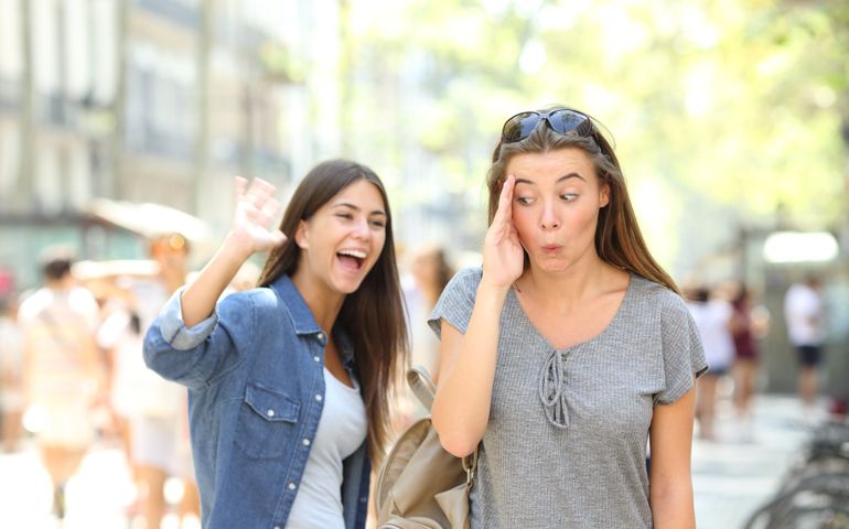 Happy teen greeting waving hand and friend ignoring her in the street