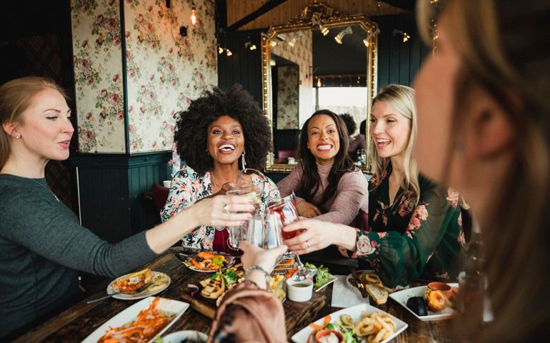 An over the shoulder shot of a group of beautiful mid-adult women enjoying a celebratory toast together in a bar.