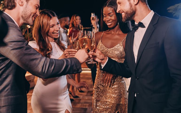 Group of people in formalwear toasting with champagne and smiling while spending time on luxury party