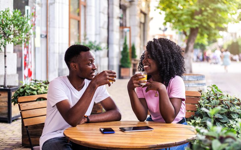 Portrait of stylish black couple talking to each other at summer street cafe.
