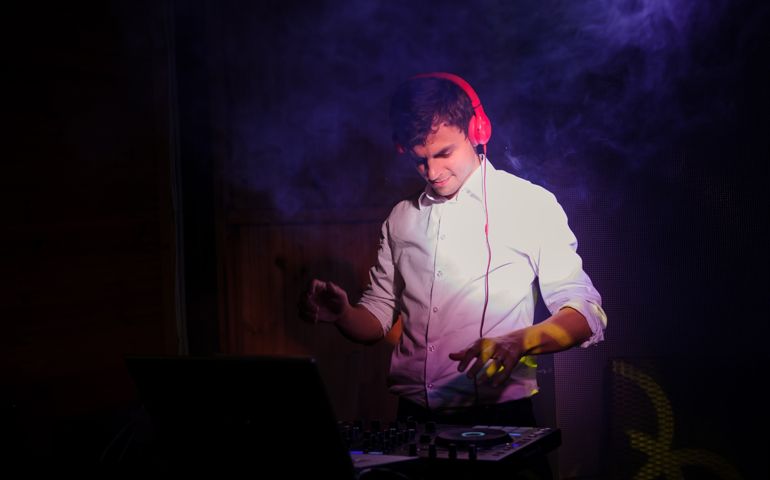 Young and beautiful man DJ/ disc jockey plays and mixing on CD players/dj mixer/mixing console at nightclub during party/ wedding party