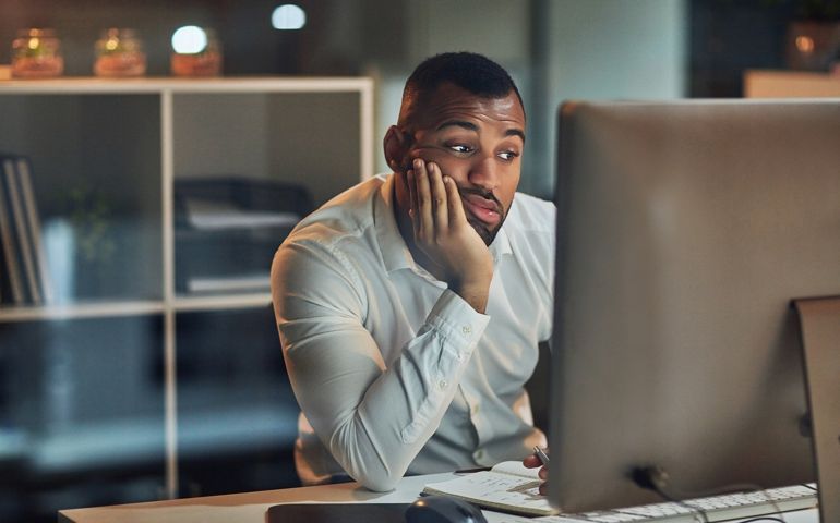 Shot of a young businessman looking bored while working at his desk during late night at work