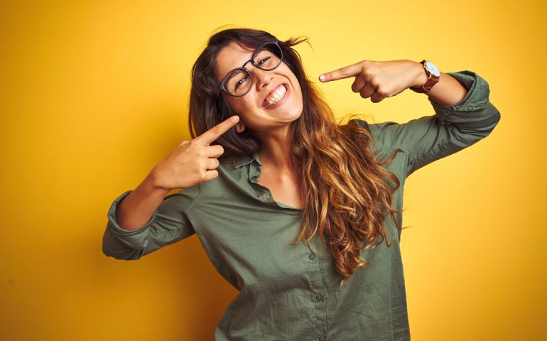 Young beautiful woman wearing green shirt and glasses over yelllow isolated background