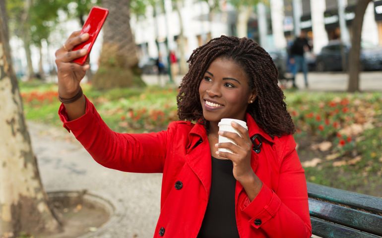 Content woman taking selfie with smartphone on street.