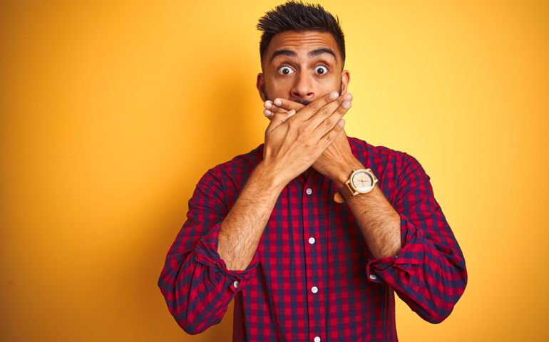 Young man wearing casual shirt standing over isolated yellow background shocked covering mouth with hands for mistake.