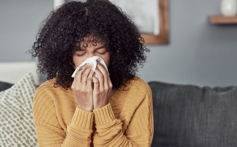 Shot of a young woman blowing her nose with a tissue at home