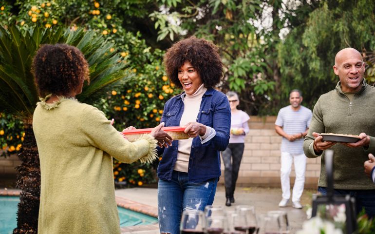 Smiling friends walking into backyard party with trays of food