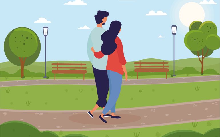 Young couple of man and woman walking together in green park. Couple in love. Girl hugging her boyfriend.