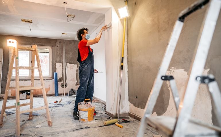 Construction worker plastering and smoothing concrete wall in room. Renovating apartment.