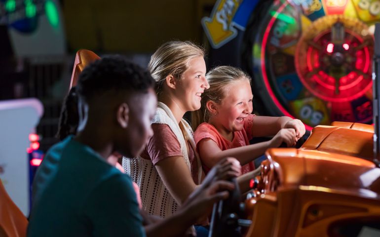 Two sisters having fun at an amusement arcade, playing an auto racing game. The girl holding the steering wheel is 6 years old and her sister is a 14 year old teenager.