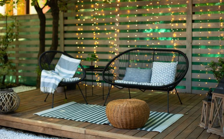 Terrace house with plants, wooden wall and table, comfortable sofa, armchair and lanterns.