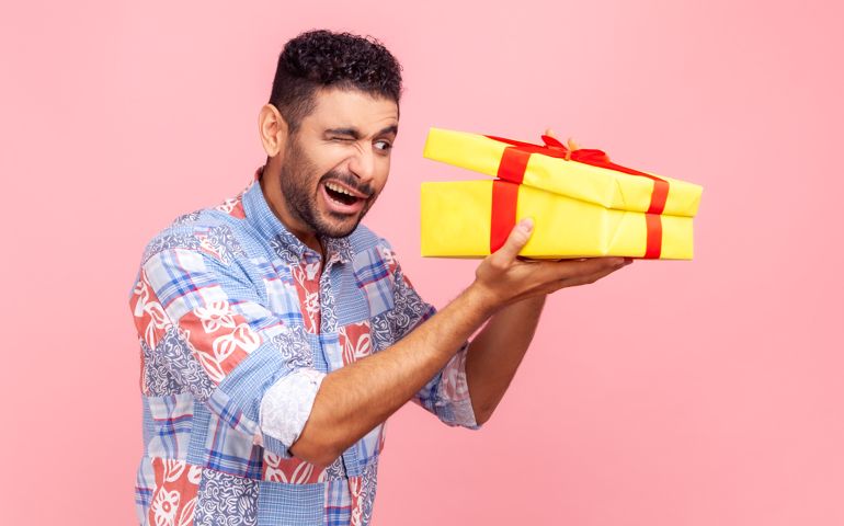 Portrait of curious happy man opening gift, peeking inside box with nosy look, unpacking present