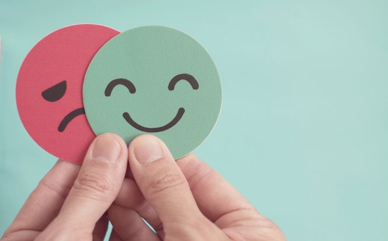 Hands holding sad face hiding behind happy face