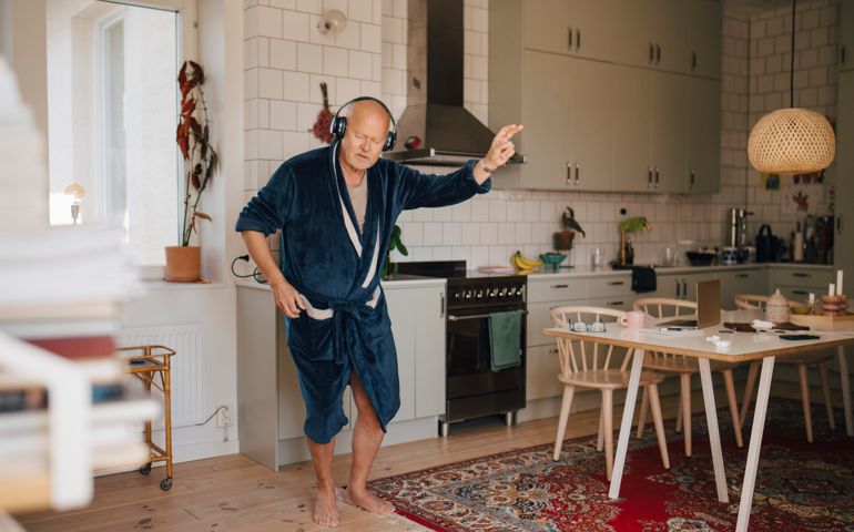 Senior man dancing while enjoying music through headphones in kitchen