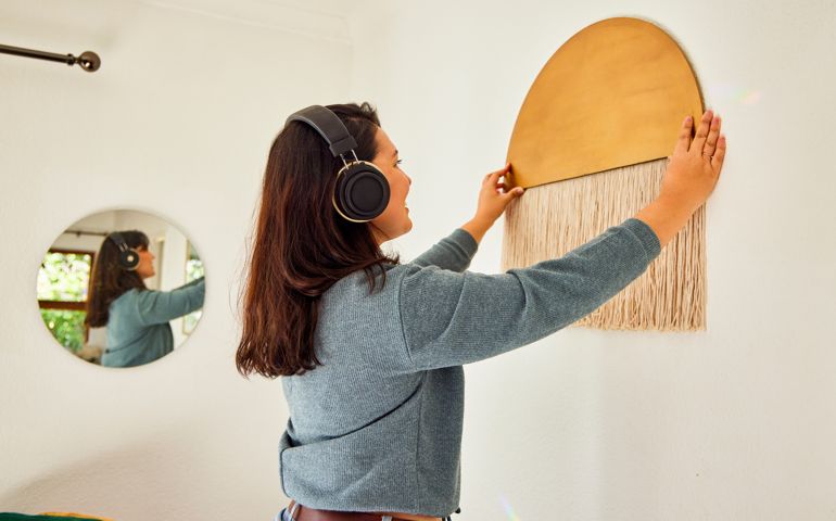 Shot of a young woman rearranging her living room at home while listening to music through headphones