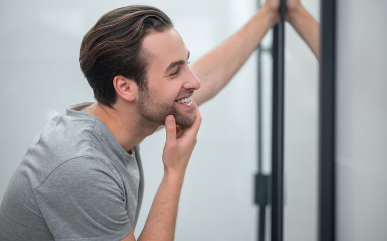 A young man in grey tshirt looking at his reflection in the mirror