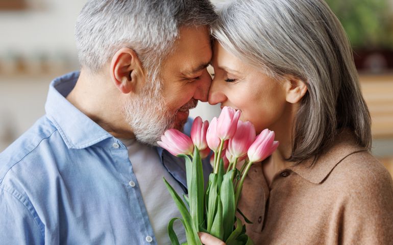 Elderly couple in love hugging on Valentine's day. A loving husband gives his wife a bouquet of tulip