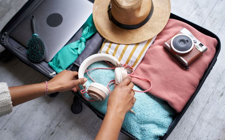 Photo of an open luggage filled with summer items ready to go on holidays, woman's black arms organizing it.