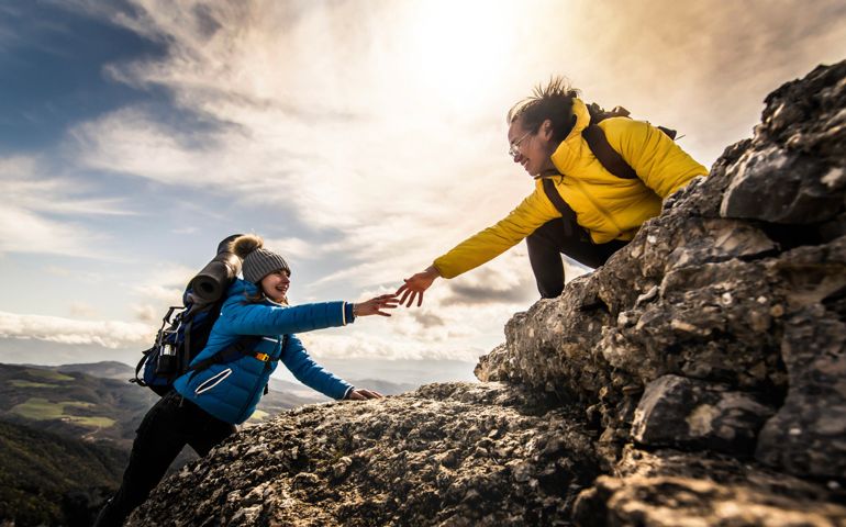 People helping each other hike up a mountain at sunrise - Giving helping hand and teamwork concept