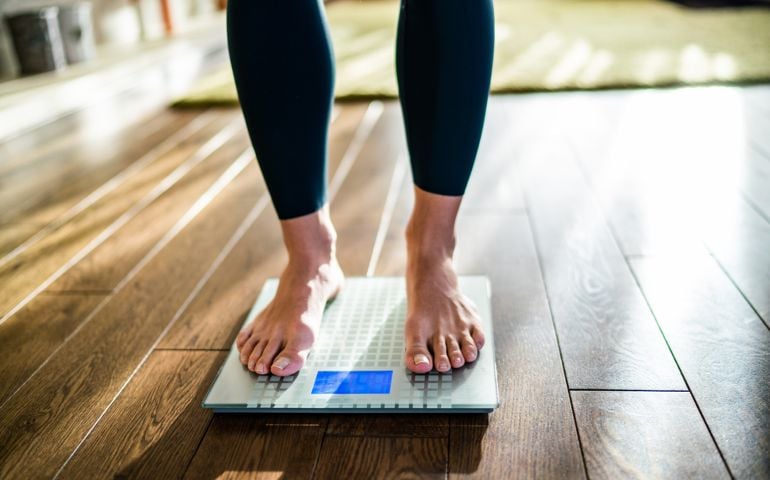 Low section of woman checking her weight on the scale at home