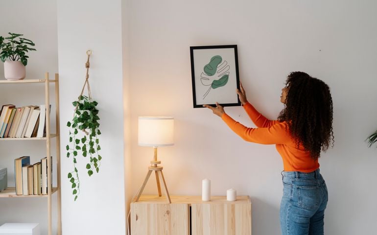 Young woman with curly hair hanging picture frame on wall at home