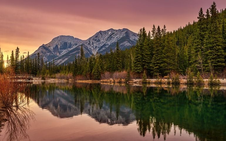 A warm sunrise glowing over mountains at Mount Lorette Ponds in the springtime.