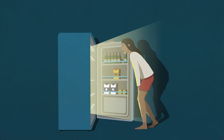 Woman standing at open refrigerator in kitchen at night