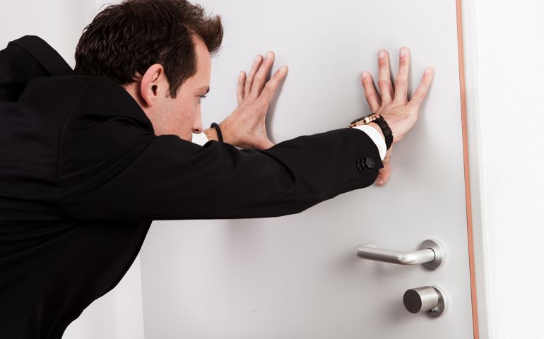 Businessman pushing the door to prevent people entering room