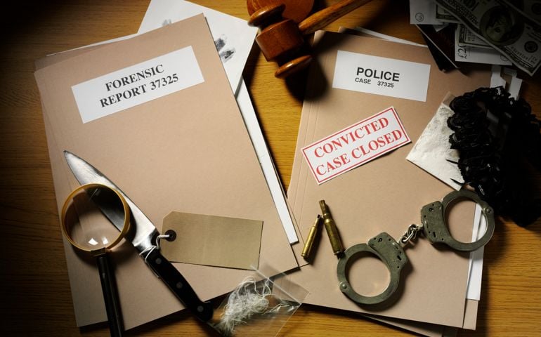 Police handcuffs, Knife and bullets on a desk with forensic and police paper files with a gavel and mallet, magnifying glass, currency and drugs. Case closed...