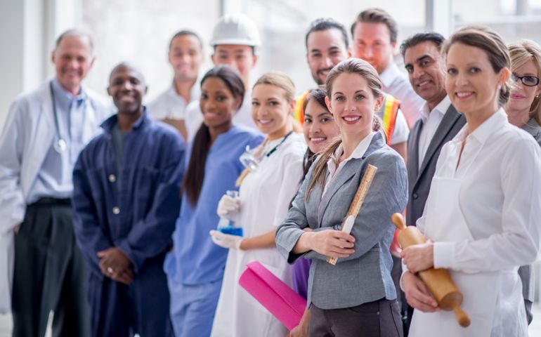 A group of varied business professionals are standing together and are smiling while looking at the camera.