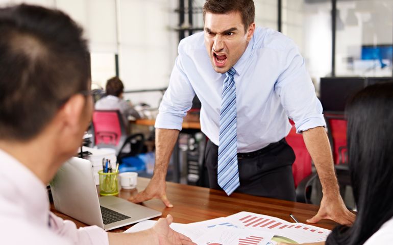 bad-tempered business executive yelling at two asian subordinates in office.